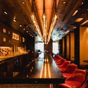 Vue de l'intérieur d'un bar restaurant CHR en difficulté, avec un long bar noir, des fauteuils rouges et des luminaires suspendus chaleureux. L'image illustre l'ambiance et le potentiel d'optimisation de l'expérience client.