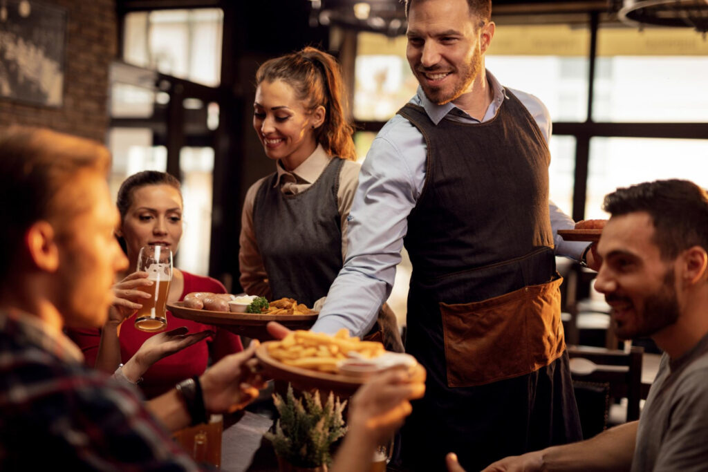 Serveur de restaurant souriant servant des clients attablés dans un bistrot chaleureux et animé